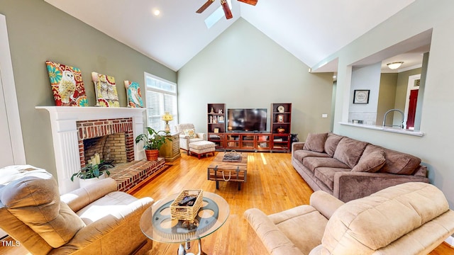 living room featuring ceiling fan, wood-type flooring, lofted ceiling with skylight, and a brick fireplace