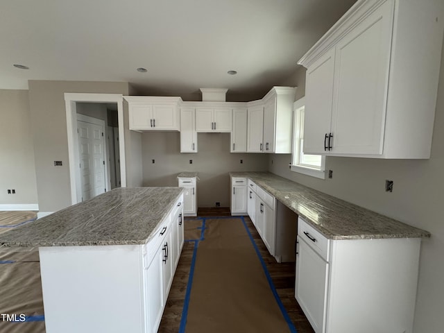 kitchen with light stone counters, white cabinetry, dark hardwood / wood-style flooring, and a kitchen island