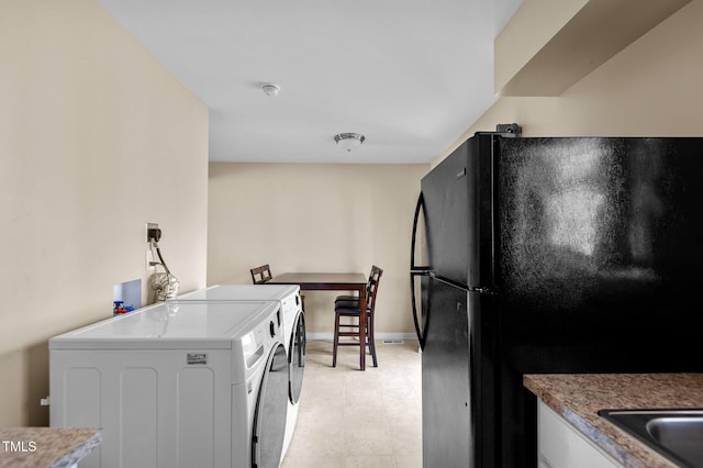 kitchen featuring black refrigerator, white cabinetry, and independent washer and dryer