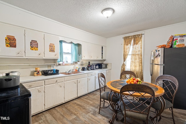 kitchen featuring stainless steel refrigerator, white cabinetry, sink, light hardwood / wood-style floors, and a textured ceiling