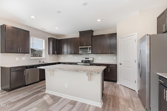 kitchen featuring dark brown cabinetry, a breakfast bar, light wood-type flooring, stainless steel appliances, and a sink