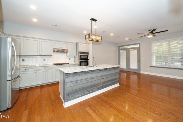 kitchen featuring stainless steel appliances, under cabinet range hood, a sink, decorative backsplash, and a ceiling fan