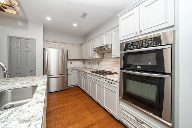 kitchen featuring stainless steel appliances, under cabinet range hood, a sink, wood finished floors, and recessed lighting