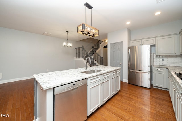 kitchen with stainless steel appliances, a sink, a chandelier, decorative backsplash, and light wood-type flooring