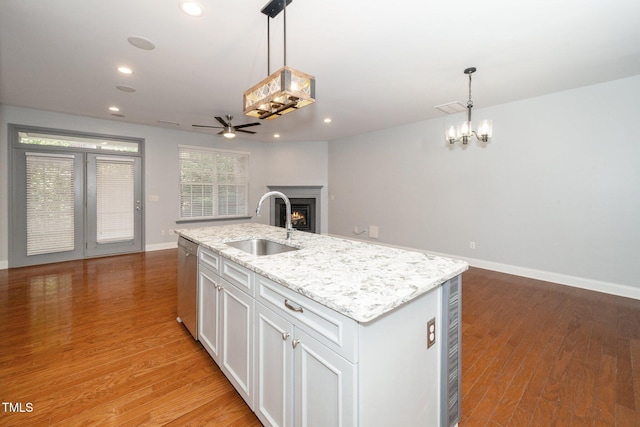 kitchen with a sink, stainless steel dishwasher, open floor plan, a warm lit fireplace, and ceiling fan