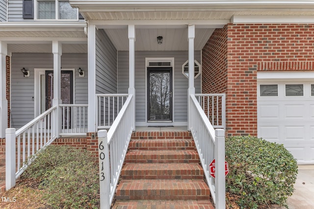 doorway to property with a garage, brick siding, and covered porch