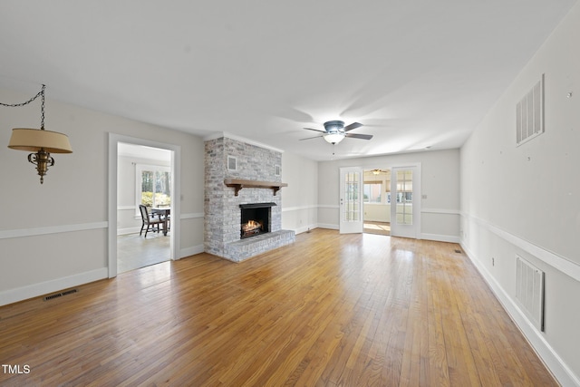 unfurnished living room with ceiling fan, a large fireplace, light hardwood / wood-style floors, and a wealth of natural light