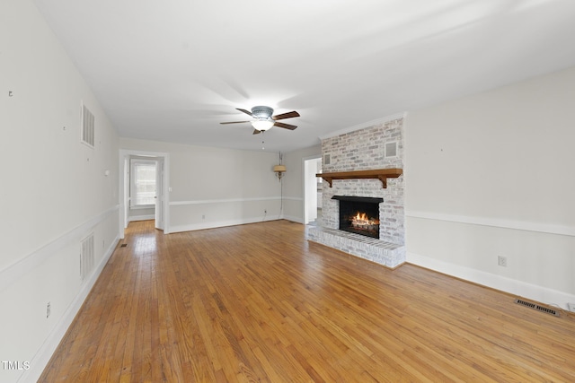 unfurnished living room with ceiling fan, a brick fireplace, and light wood-type flooring