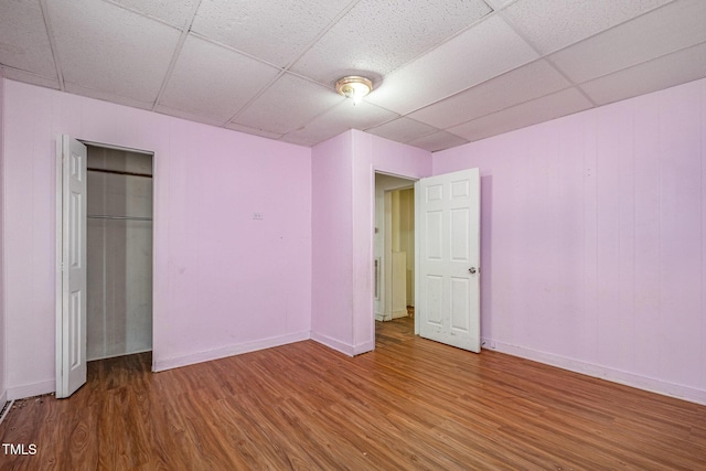 unfurnished bedroom with hardwood / wood-style flooring, a drop ceiling, and a closet