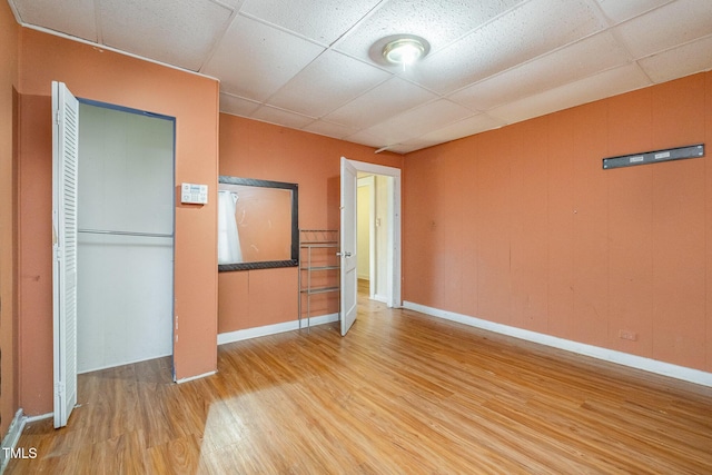 unfurnished bedroom featuring a drop ceiling, light wood-type flooring, and a closet