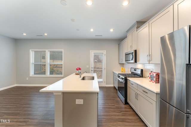 kitchen featuring appliances with stainless steel finishes, tasteful backsplash, sink, dark hardwood / wood-style flooring, and a center island with sink