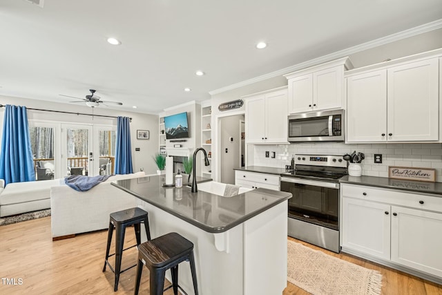 kitchen with appliances with stainless steel finishes, white cabinetry, sink, a kitchen breakfast bar, and a kitchen island with sink