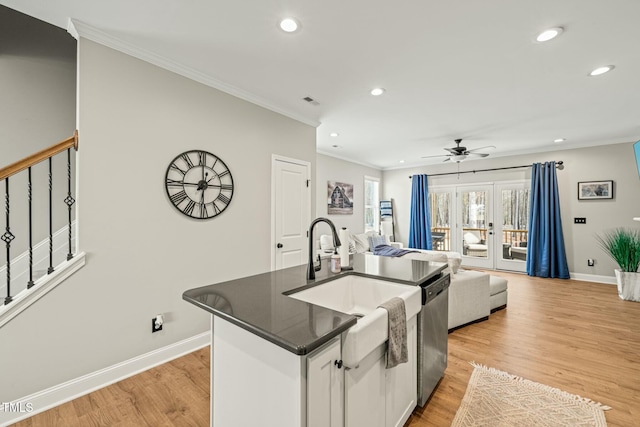 kitchen featuring white cabinets, stainless steel dishwasher, light hardwood / wood-style floors, crown molding, and a center island with sink