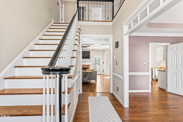 stairs featuring baseboards, a brick fireplace, wood finished floors, and a towering ceiling