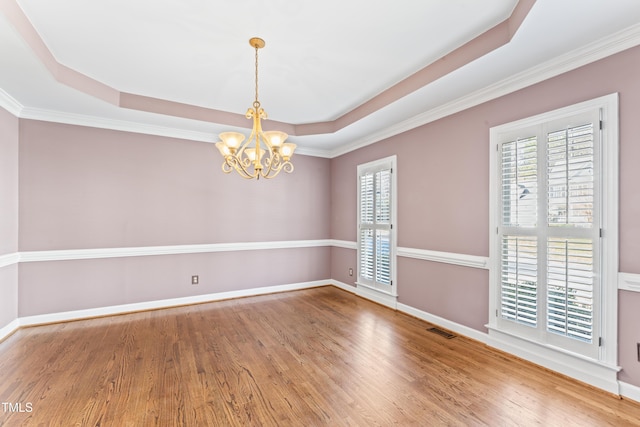 empty room with visible vents, plenty of natural light, a tray ceiling, and wood finished floors