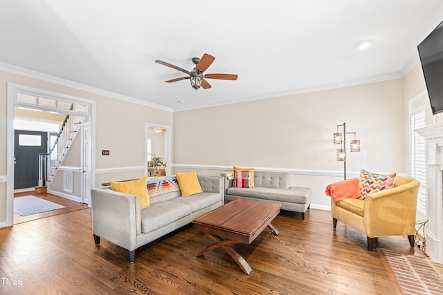 living room featuring stairway, a fireplace, wood finished floors, and crown molding