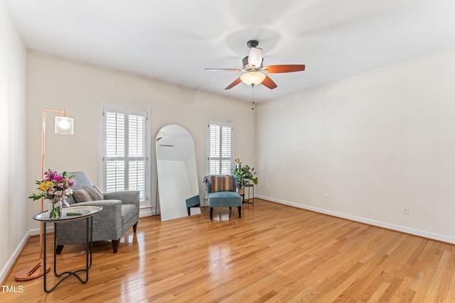 sitting room featuring light wood finished floors, arched walkways, baseboards, and ceiling fan