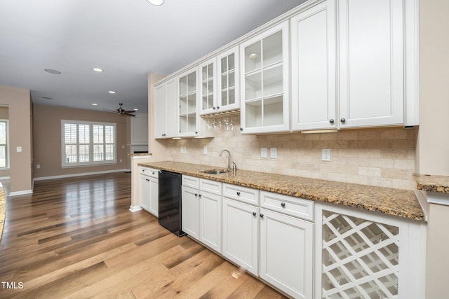 kitchen featuring a sink, white cabinetry, black dishwasher, light wood finished floors, and tasteful backsplash