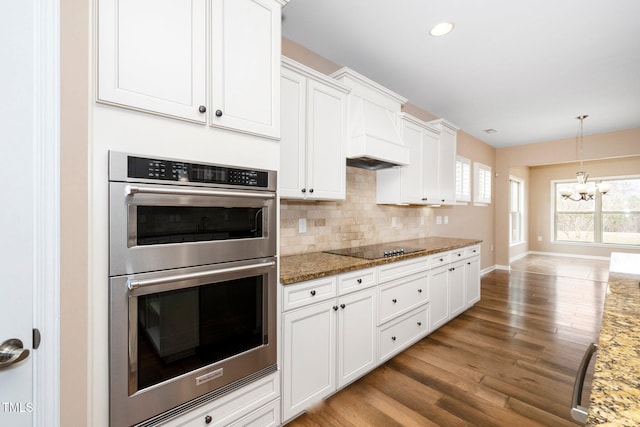 kitchen featuring double oven, black electric stovetop, light stone counters, light wood-style flooring, and decorative backsplash