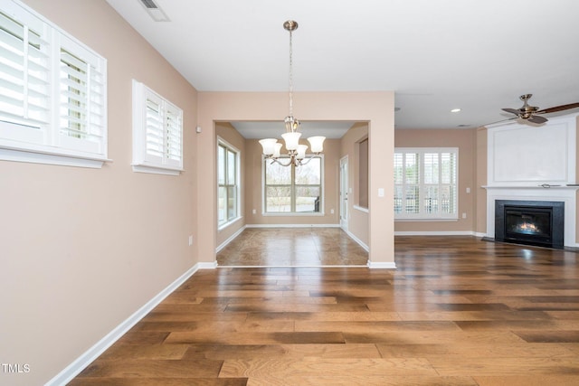 unfurnished dining area featuring wood finished floors, a fireplace with flush hearth, visible vents, and baseboards