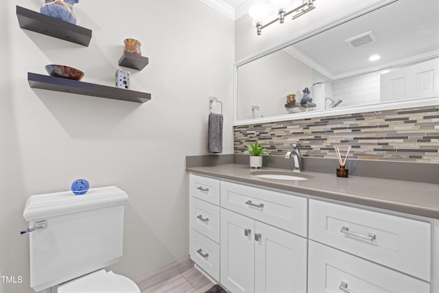 bathroom with tasteful backsplash, ornamental molding, toilet, and vanity