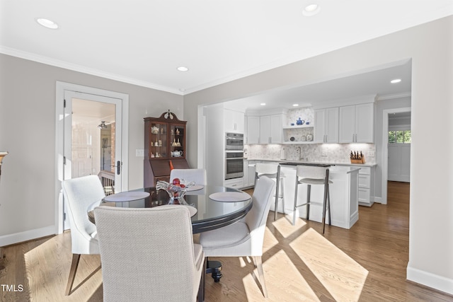 dining space with crown molding, sink, and light wood-type flooring