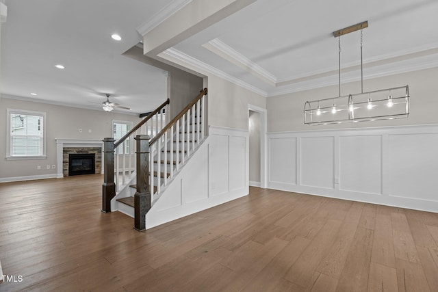 interior space with a stone fireplace, wood-type flooring, ornamental molding, and ceiling fan