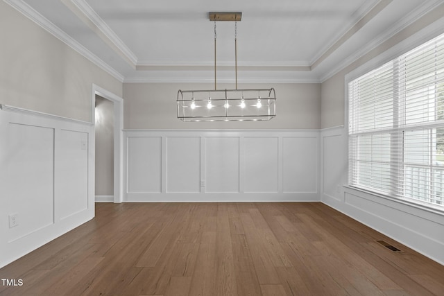 unfurnished dining area with a raised ceiling, ornamental molding, and hardwood / wood-style floors