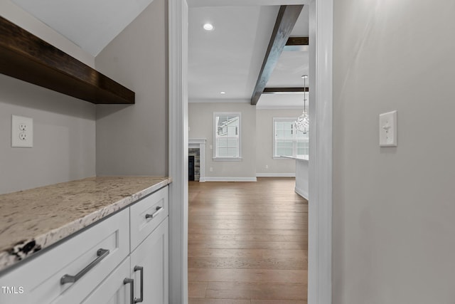 kitchen featuring dark wood-type flooring, white cabinetry, light stone counters, decorative light fixtures, and beam ceiling