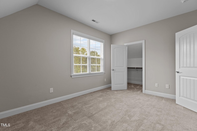 unfurnished bedroom featuring a walk in closet, lofted ceiling, light colored carpet, and a closet