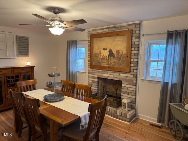 dining space featuring ceiling fan, a fireplace, wood-type flooring, and plenty of natural light