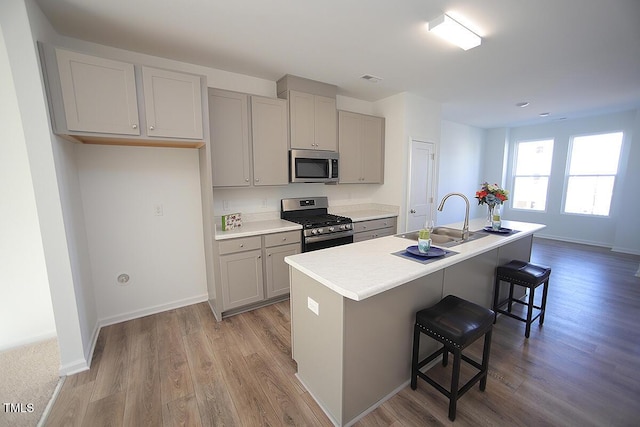 kitchen with sink, gray cabinetry, appliances with stainless steel finishes, a kitchen breakfast bar, and an island with sink