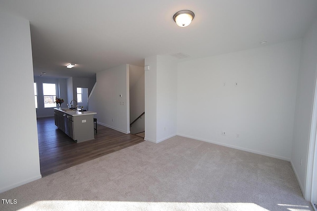 interior space featuring dark colored carpet, a kitchen island with sink, and sink