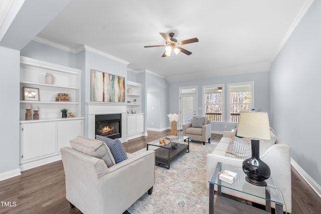 living room featuring baseboards, ornamental molding, wood finished floors, and a glass covered fireplace