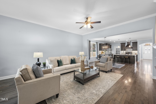 living area with baseboards, ornamental molding, dark wood-style flooring, and ceiling fan with notable chandelier