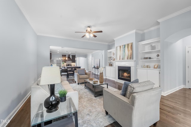 living room with arched walkways, light wood-style flooring, ornamental molding, a warm lit fireplace, and baseboards