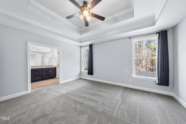 unfurnished bedroom with connected bathroom, light colored carpet, baseboards, a tray ceiling, and crown molding