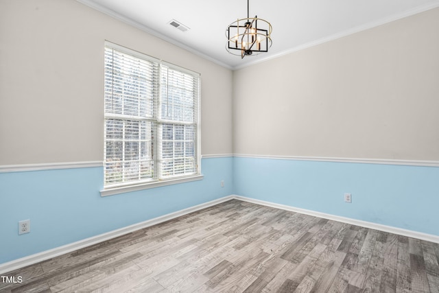 spare room featuring baseboards, visible vents, wood finished floors, crown molding, and a chandelier