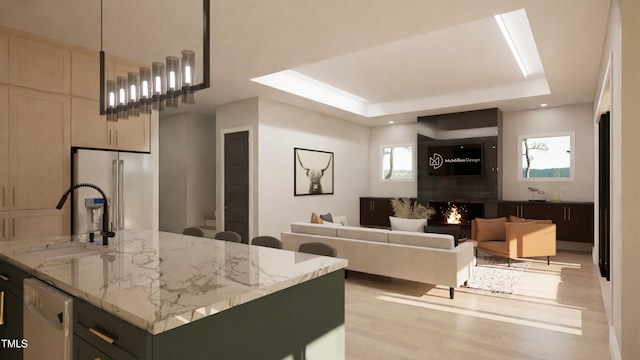 kitchen featuring sink, dishwasher, a kitchen island with sink, a tray ceiling, and light stone countertops