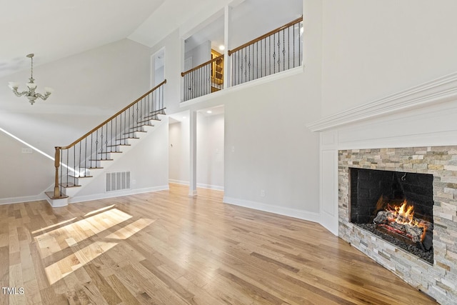 unfurnished living room featuring wood-type flooring, a stone fireplace, a notable chandelier, and high vaulted ceiling