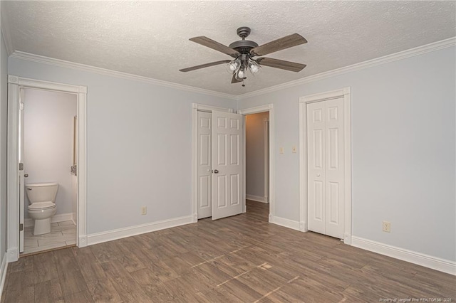 unfurnished bedroom with dark hardwood / wood-style floors, ensuite bath, ornamental molding, ceiling fan, and a textured ceiling