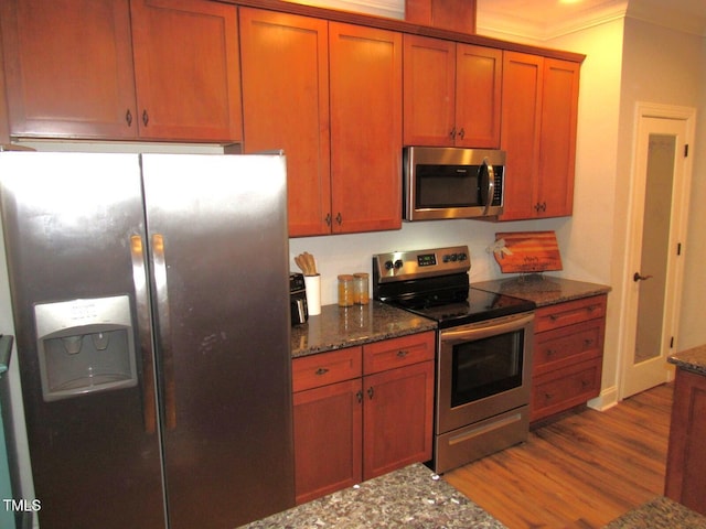 kitchen featuring ornamental molding, appliances with stainless steel finishes, light hardwood / wood-style flooring, and dark stone counters