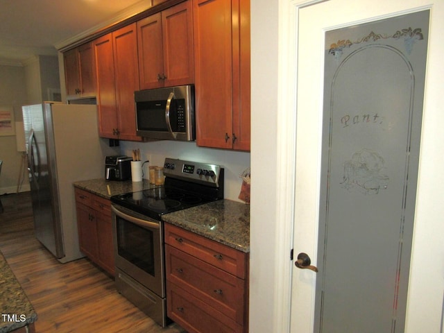 kitchen with stainless steel appliances, dark stone counters, and light wood-type flooring