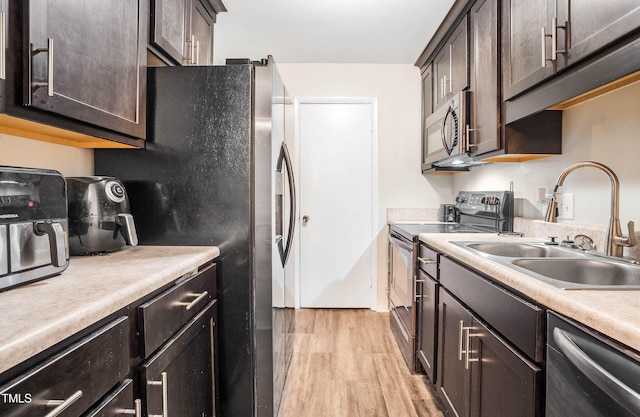 kitchen with light wood finished floors, dark brown cabinets, light countertops, appliances with stainless steel finishes, and a sink