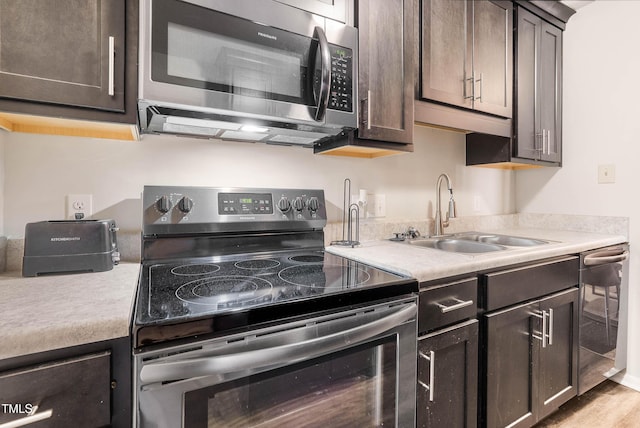 kitchen featuring light countertops, dark brown cabinets, appliances with stainless steel finishes, and a sink