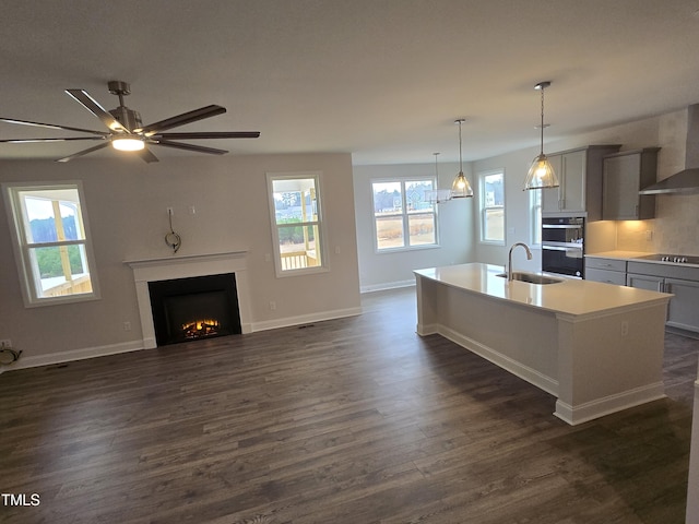 kitchen with sink, hanging light fixtures, gray cabinets, an island with sink, and wall chimney range hood