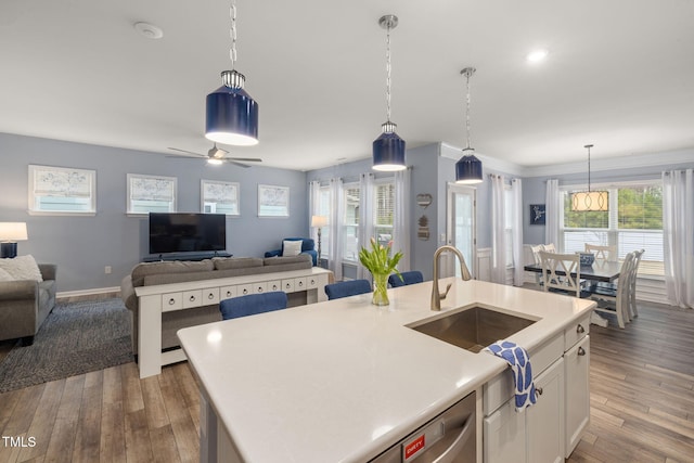 kitchen with sink, hanging light fixtures, wood-type flooring, white cabinets, and a center island with sink