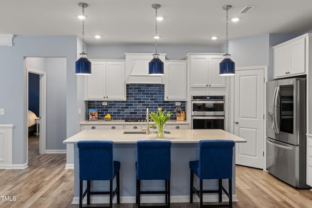 kitchen with pendant lighting, white cabinetry, decorative backsplash, stainless steel appliances, and a center island with sink