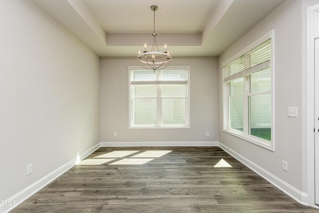 unfurnished dining area with baseboards, wood finished floors, a chandelier, and a tray ceiling