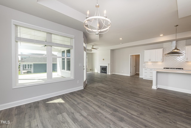 unfurnished living room featuring baseboards, recessed lighting, a fireplace, dark wood-type flooring, and ceiling fan with notable chandelier